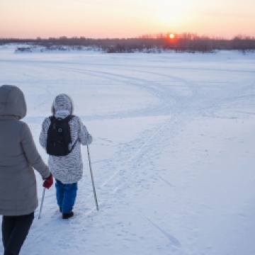 Two older women walking through snow using poles for balance